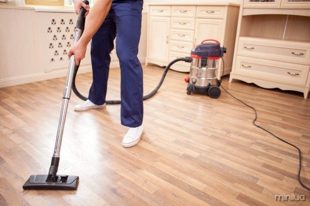 Close up of male legs standing in a room. The man is vacuuming floor in his house
